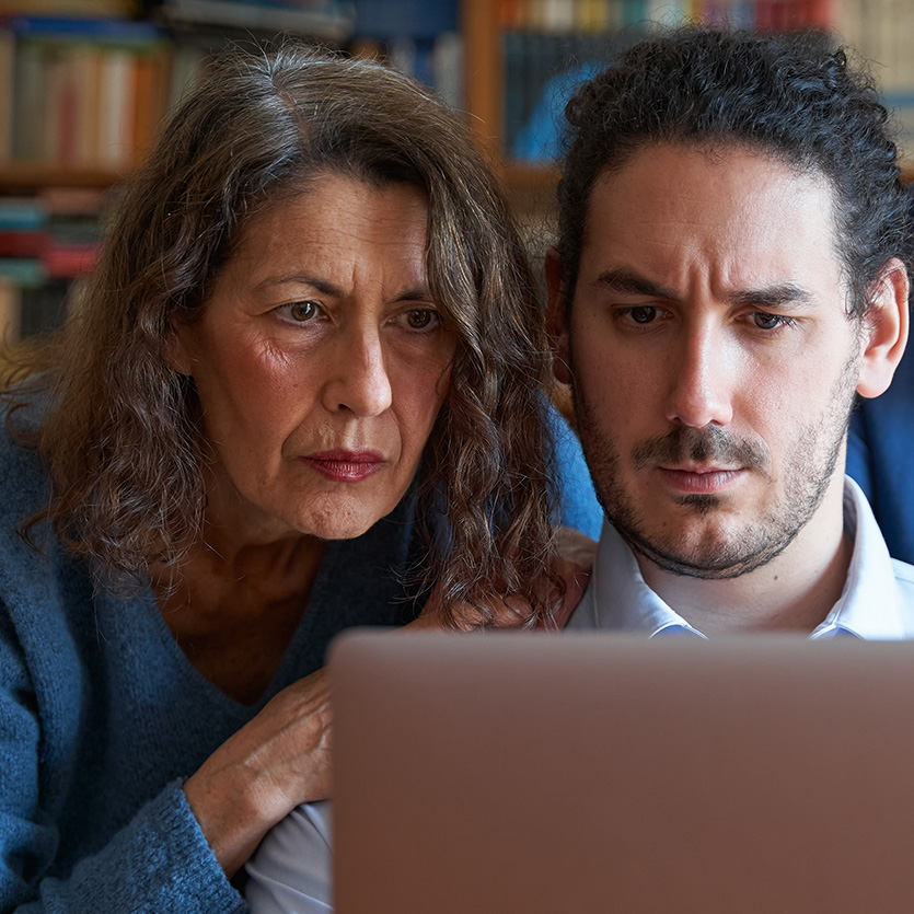 Mutter mit erwachsenem Sohn vor Laptop mit verzweifeltem Gesichtsausdruck
